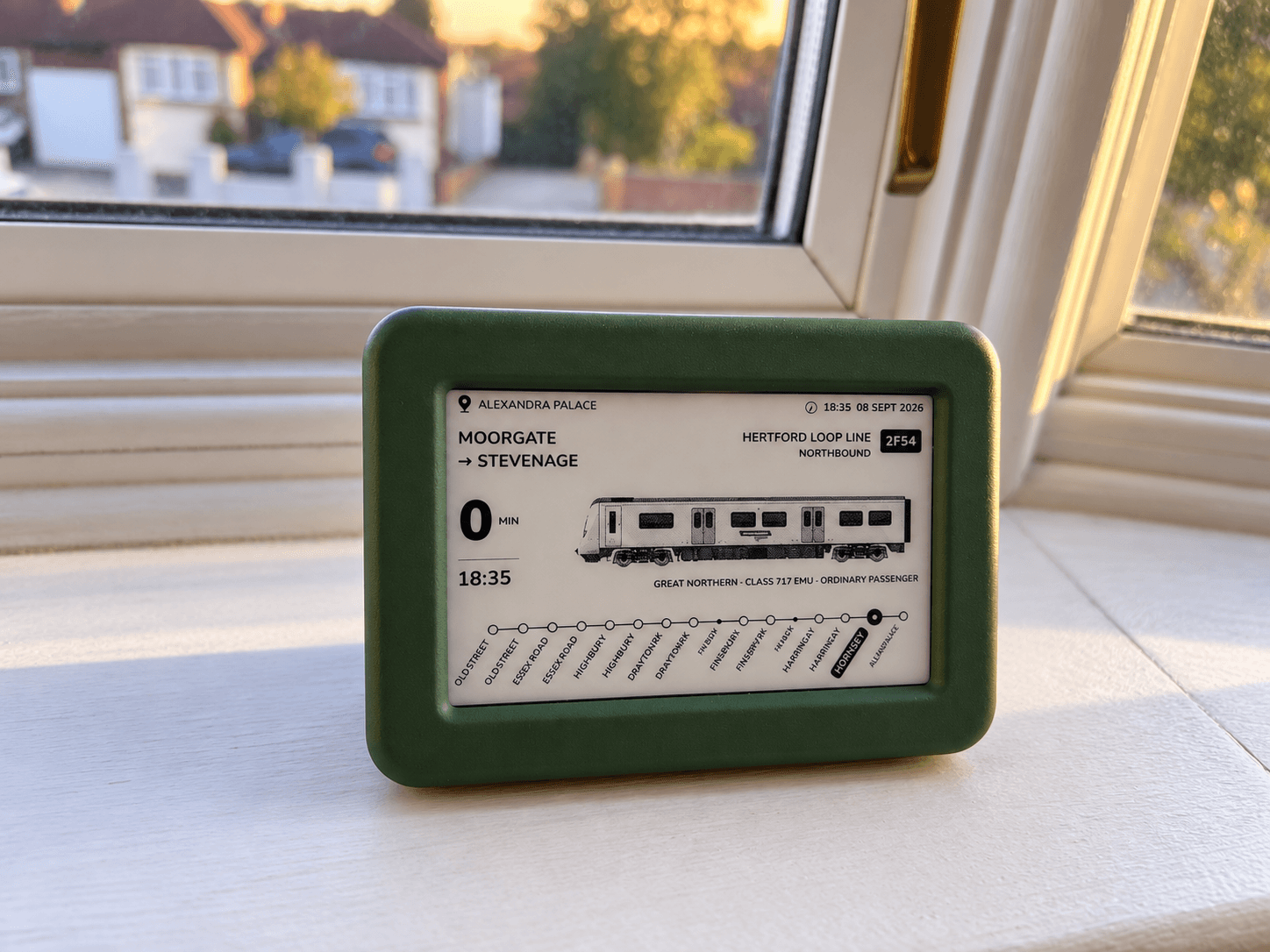 The green Lineside Ink display on a sunlit windowsill, showing a Great Northern train reaching Alexandra Palace on the Hertford Loop Line.