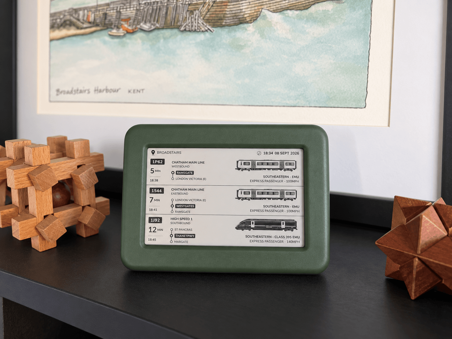 The green Lineside Ink display on a shelf below a framed Broadstairs Harbour print, its e-paper screen listing three approaching Southeastern services at Broadstairs.